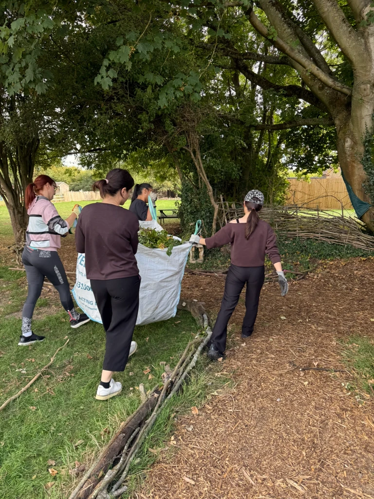 Volunteers carrying a large bag of garden waste across the woodland area