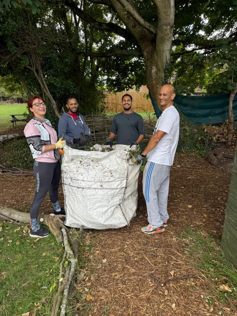 Four volunteers smiling beside a large bag filled with cleared undergrowth