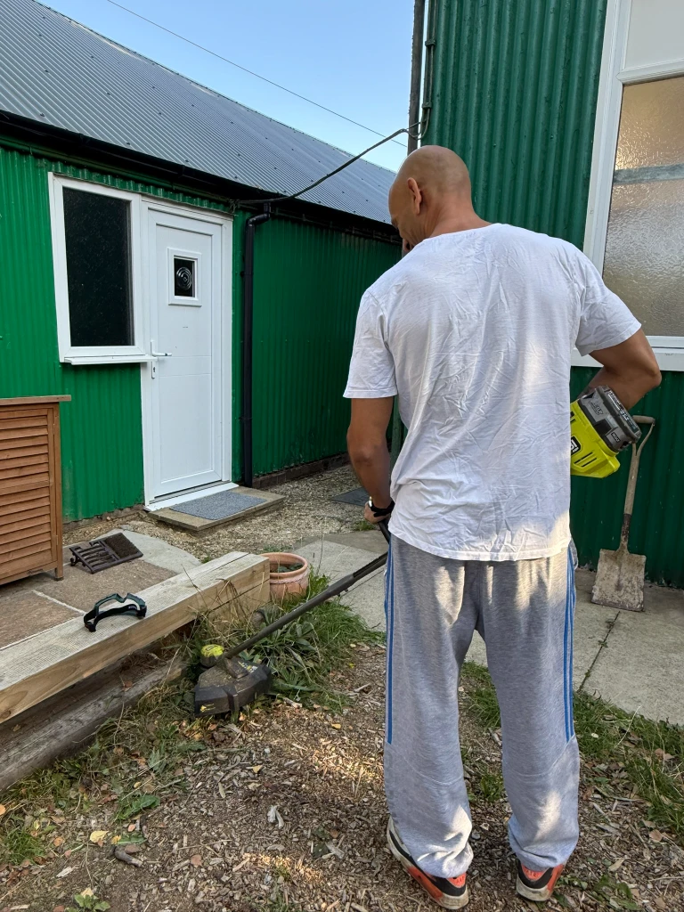 A volunteer strimming grass along the path outside the centre