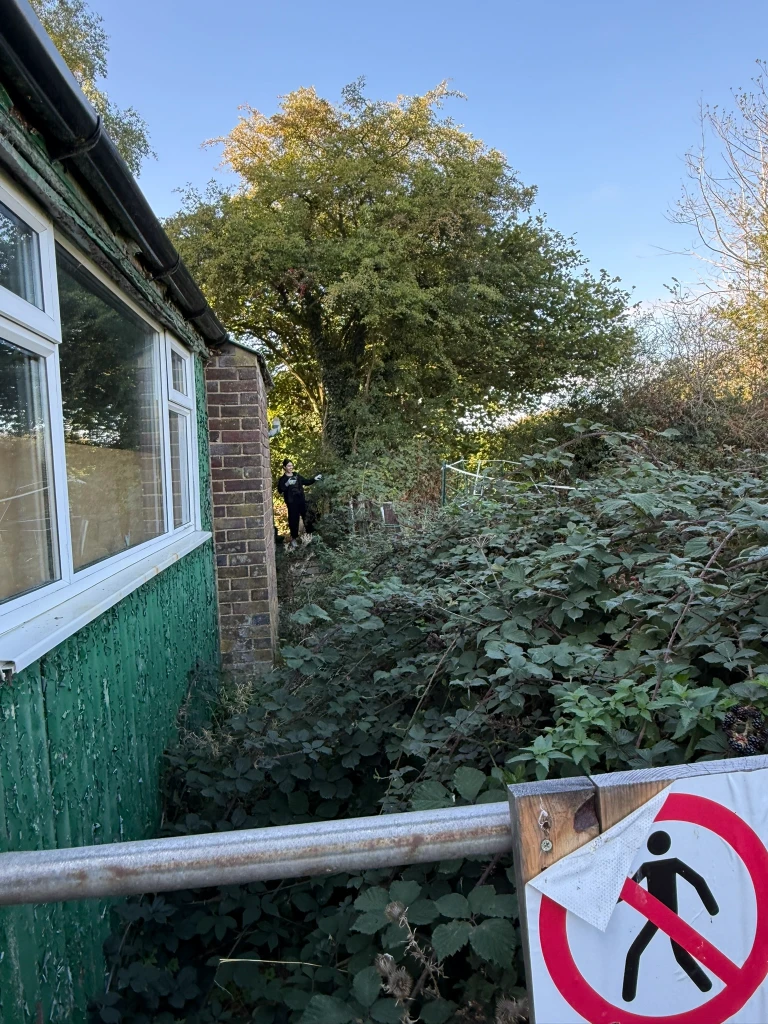 Dense brambles alongside the building, with a volunteer starting to clear the far end